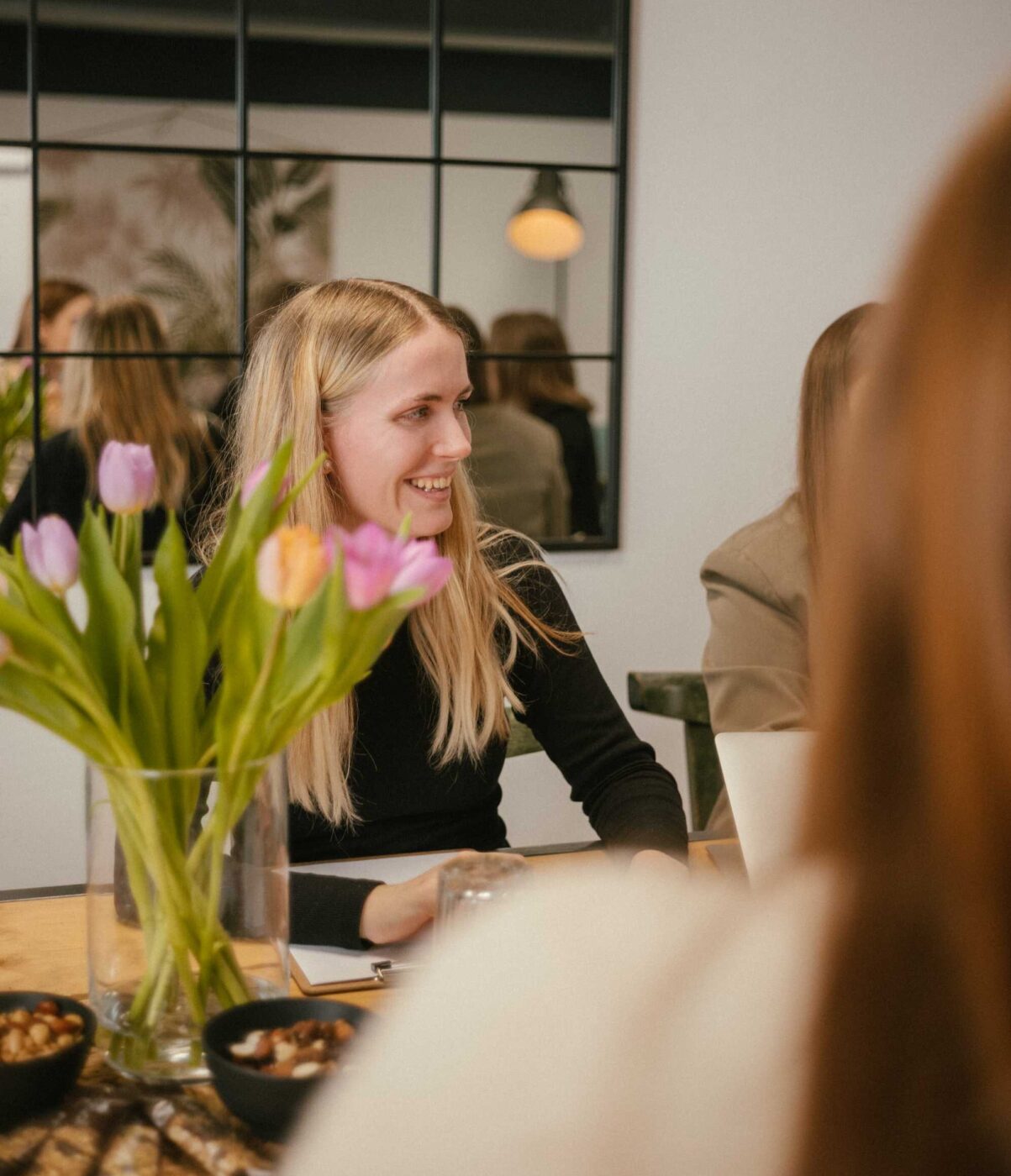 Frau sitzt am Tisch mit Tulpen, lacht und schaut zur Seite
