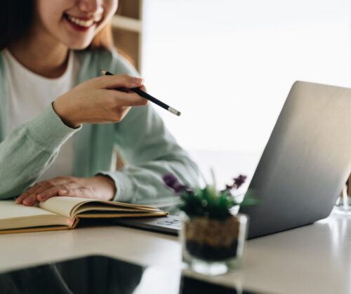Frau lächelt und zeigt mit Stift auf Laptop