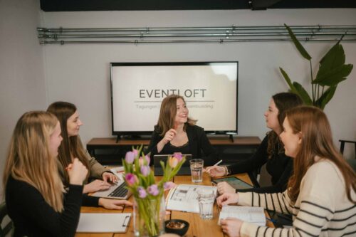 5 Frauen sitzen an einem Tisch im Eventloft bei einer Besprechung